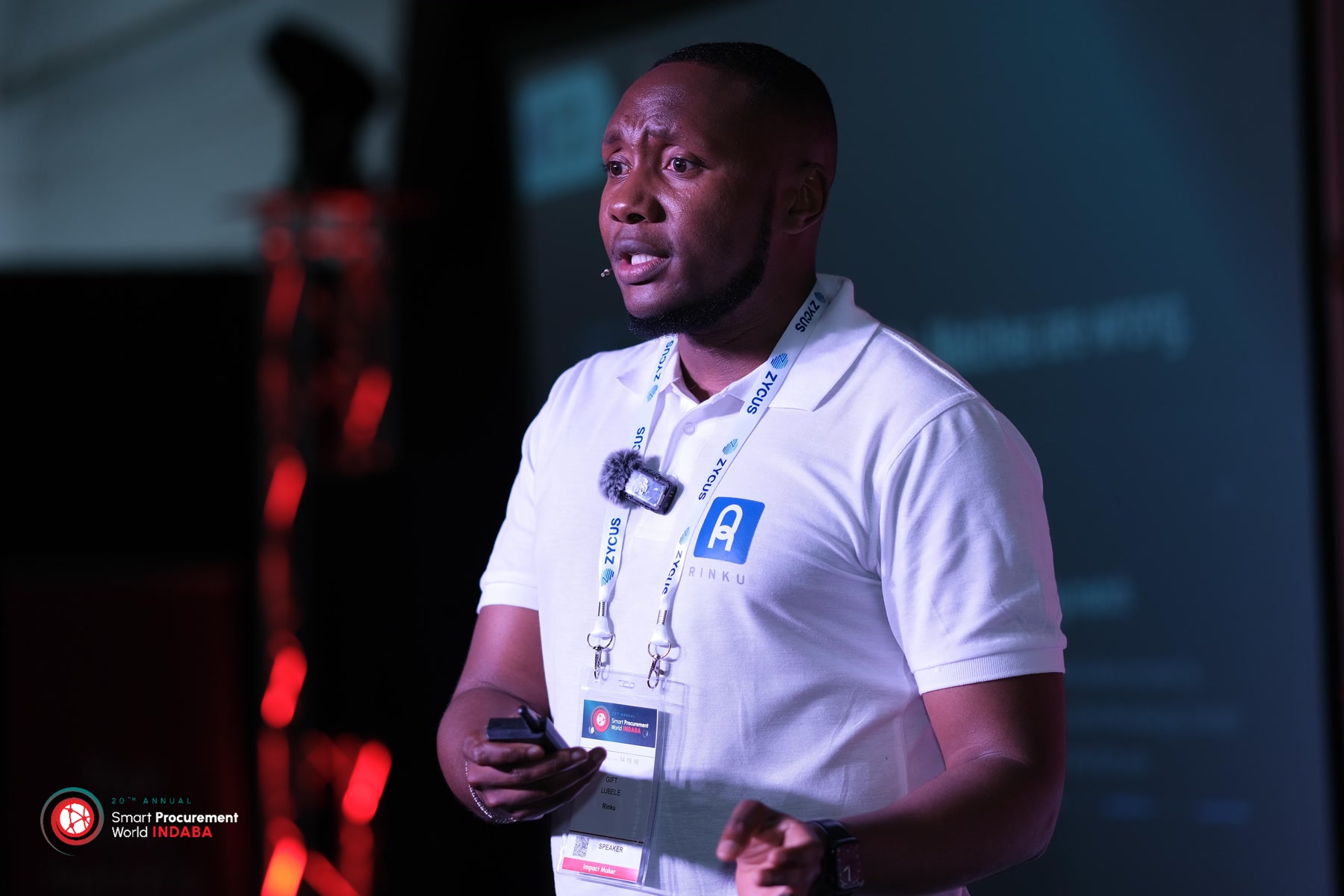 Gift Lubele speaking at the 20th Annual Smart Procurement World Indaba, Rinku polo and speaker badge, clicker in hand. Photograph.