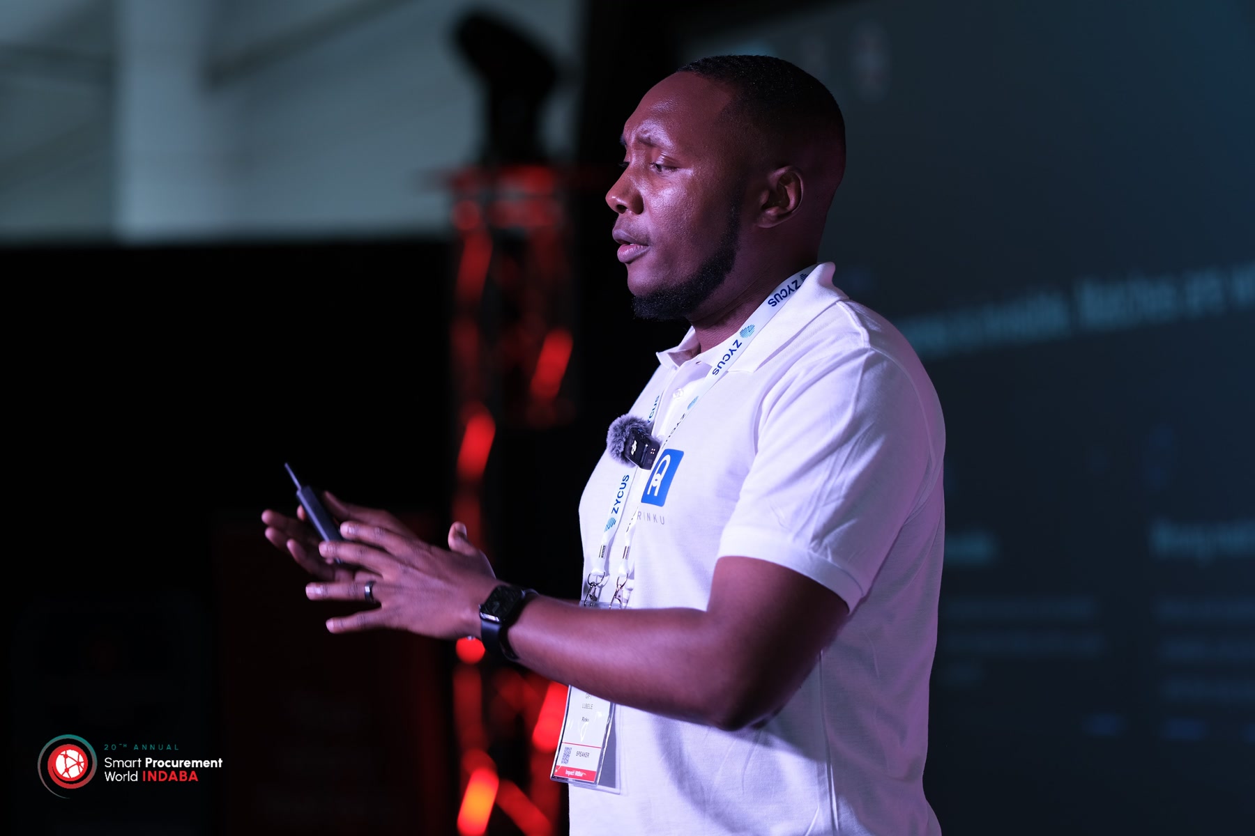 Gift Lubele in profile on stage at Smart Procurement World Indaba, clicker in both hands. Photograph.